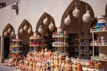 A lively Middle Eastern pottery market showcasing rows of handmade terracotta vases, ceramic lanterns, and colorful clay crafts under arched Arabic architecture