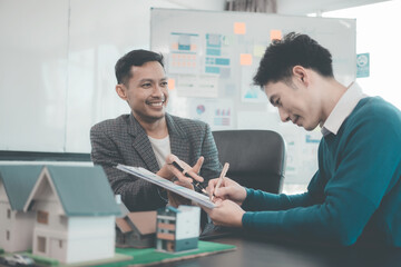 A group of young Asian businesspeople meet at an office for a residential real estate project. A group of elegant, professionally dressed individuals evaluate a small house model.