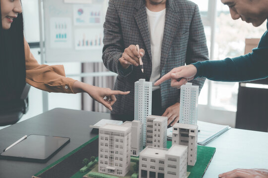 A group of young Asian businesspeople meet at an office for a residential real estate project. A group of elegant, professionally dressed individuals evaluate a small house model.