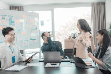 Group of successful Asian businesspeople smiling and laughing, posing and making gestures of joy together in a company office conference room.