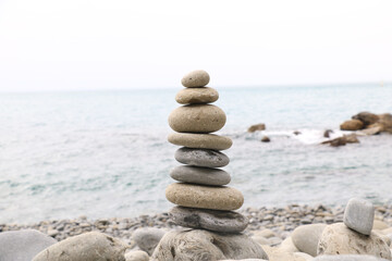 Fototapeta premium Balanced stones stacked on the beach with calm sea background, symbolizing harmony, balance, and mindfulness in nature. Perfect concept for wellness, meditation, and tranquility themes.