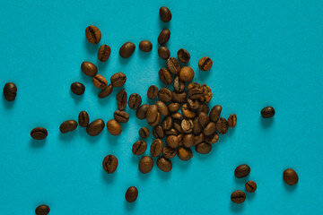 Scattered roasted coffee beans on a vibrant turquoise background create a bold visual contrast. The rich brown tones and organic shapes evoke themes of aroma, energy, and artisanal coffee culture.
