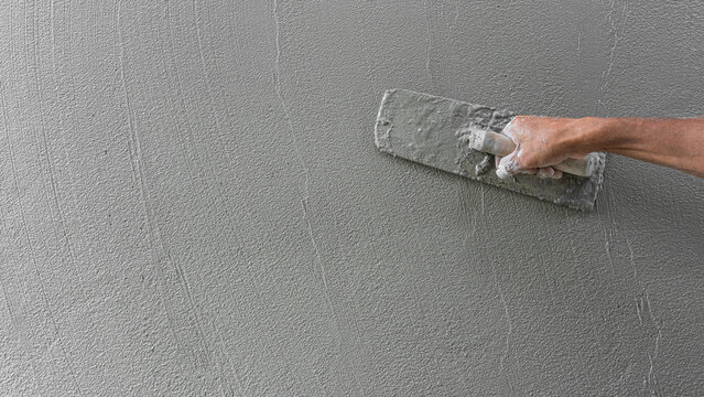 Hand worker plaster grey cement wall texture background with holding trowel handle, Concrete mortar wet construstion house site well free space groud for text presentation