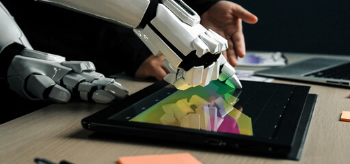 A robotic hand engages with a tablet showcasing vibrant data visuals, symbolizing advanced technology integration in a modern office setting.Noogenesis