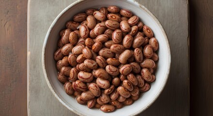 Fototapeta premium Dry pinto beans in a rustic bowl, top view on a dark wooden background with copy space. Raw, uncooked speckled legumes, a staple ingredient for healthy Mexican cuisine and high fiber diets