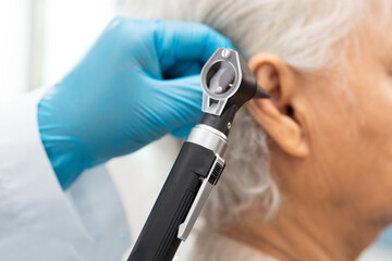 Audiologist or ENT doctor use otoscope checking ear of asian senior woman patient treating hearing...