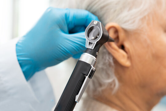 Audiologist or ENT doctor use otoscope checking ear of asian senior woman patient treating hearing loss problem.