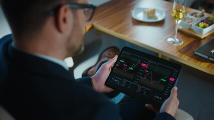 Over-the-shoulder view of a financial analyst in a suit checking cryptocurrency or stock market charts on a tablet, traveling in a business class lounge or a private jet - Powered by Adobe