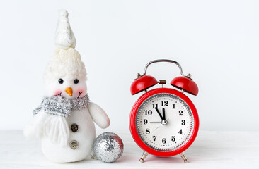 A snowman toy and bright red alarm clock shows five minutes to midnight on a white background.