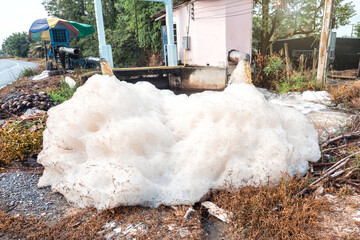 Murky foam piles created by floating fast from flow of polluted water from a large water pump to accelerate drainage after rain at irrigation canal gate along village road in rural Thailand.