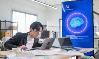 Asian businessman working on laptop in modern office, using smartphone voice recognition and AI...