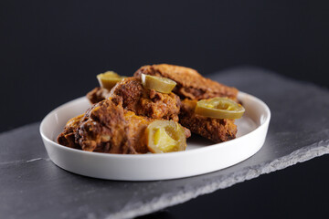 Closeup Crispy fried chicken wings with pickles on white plate rock against dark background
