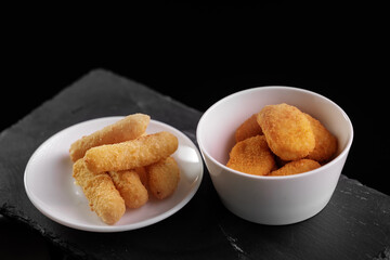 Assorted golden fried snacks in bowls on dark surface, top view