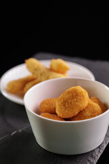 Golden chicken nuggets and potato wedges in white bowls on slate surface, top view