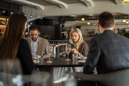 Business colleagues using phones at a restaurant table during a meeting - Powered by Adobe