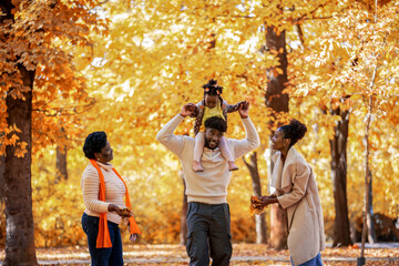 African American Family Walking in Autumn Park with Girl on Dad’s Back