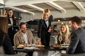 Restaurant staff serving food to a group of happy customers at a table