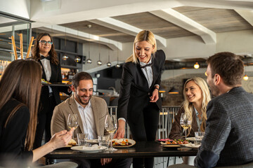 Restaurant staff serving food to a group of happy customers at a table