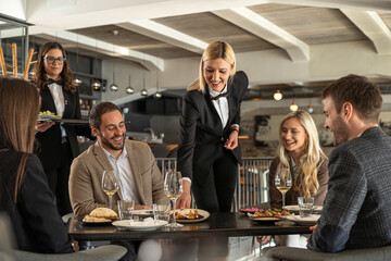Restaurant waiter serving food to happy customers at a dining table