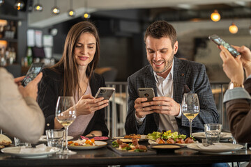 Friends enjoying a meal at a restaurant while using their smartphones