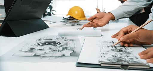 Engaged team discussing technical drawings and project plans in a bright office environment. Essential tools and documents are visible, highlighting collaborative effort. SACTR