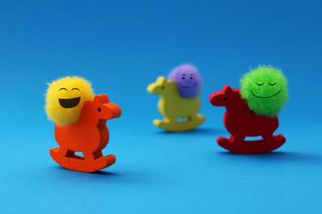 Three rocking wooden horses, each with a smiling plush sphere