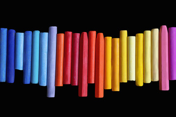 Row of different colorful oil pastel crayons isolated on black. Flat lay