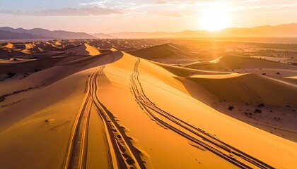 Golden Desert Dunes Under Sunset Sky with Tire Tracks and Distant Hills Creating a Vast Arid Landscape from a High Vantage Point