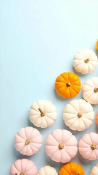 Colorful mini pumpkins: orange, white, and pink hues arranged diagonally on a pale blue surface with soft lighting.