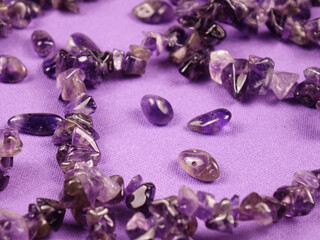 Amethyst bead necklace lies on a purple cloth, top view, background