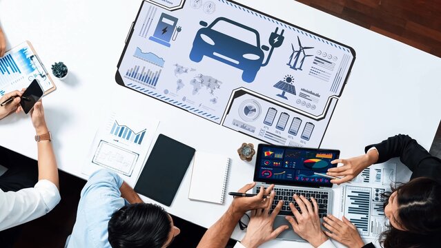 Group of professionals collaborating on automotive innovation using digital analytics and data visualization tools in a modern office setting, highlighting teamwork. Raster
