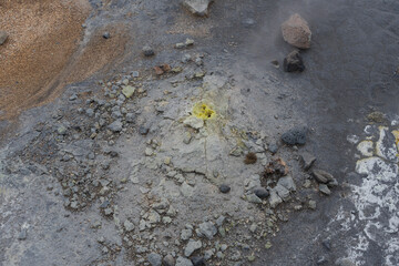 Volcanic terrain with rocks, ash, and yellow sulfur deposits steaming out.
