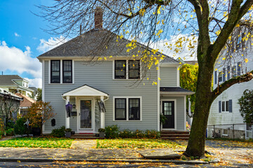 Charming two-story family house with light gray siding on a sunny autumn day in Brighton, Boston,...