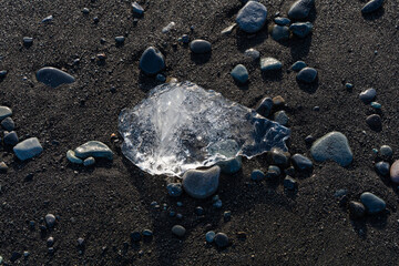 Crystal ice gleams on volcanic beach, dark sand, smooth stones abound.