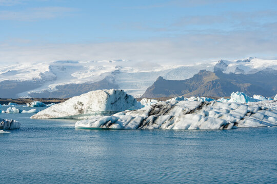 Icebergs floating in a glacial lagoon, with mountains in the background. - Powered by Adobe
