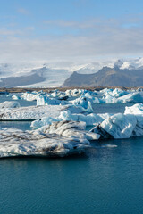 Floating icebergs dot a serene glacial lagoon, mountains in the distance.