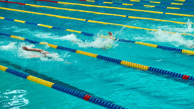 Swimmers competing in a race at an indoor pool with blue and yellow lane dividers. Action shot capturing splashes and movement in clear turquoise water