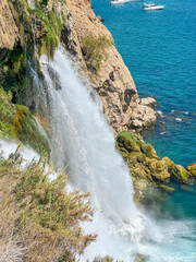 Duden Waterfall dramatically plunging from rocky cliffs into turquoise Mediterranean Sea near coastal vegetation in Antalya, Turkey. High quality photograph