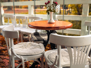 cozy outdoor cafe terrace with white wooden chairs and small round table in autumn
