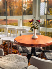vertical shot of cozy empty cafe terrace table with roses and autumn background