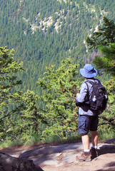 Male hiker stands on the edge of a mountain and admires the forested view of the Rocky Mountains in Banff National Park, Alberta, Canada