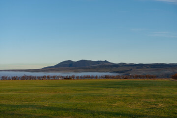 Fototapeta premium A serene landscape featuring a green field, mountains, and a clear blue sky.