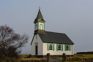 Fototapeta premium Quaint white church with green accents in serene, overcast landscape.