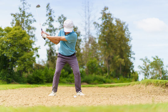 Asian male golfer hitting bunker shot from sand.