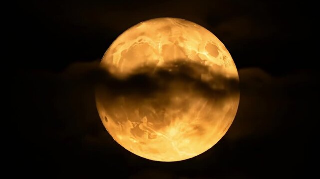 A captivating full celestial body glows with a warm, radiant golden-orange hue, dominating the dark expanse of the night sky. Wispy, mysterious clouds drift slowly across its luminous surface, creatin