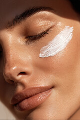 Close up detail of beautiful beauty woman with hydrating facial lotion cream smear applied on face. Skincare and cosmetics concept background.