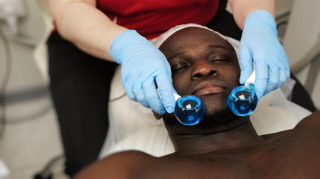 Close up of man receiving cryotherapy facial massage with ice globes in aesthetic clinic. Professional skincare treatment for face relaxation and toning.