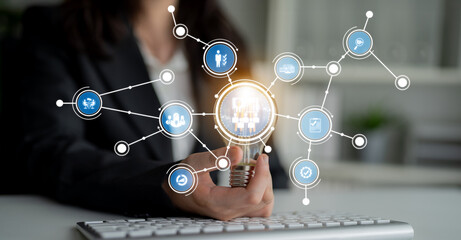 A businesswoman holds a light bulb, symbolizing ideas and innovation, surrounded by digital icons depicting technology integration in modern workplace operations. Crux