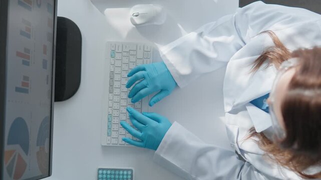 A focused researcher in a lab coat and gloves is typing on a keyboard, analyzing data displayed on a monitor. The scene captures the essence of scientific research and data analysis. - Powered by Adobe
