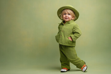 Toddler boy smiling while wearing a green outfit and hat indoors